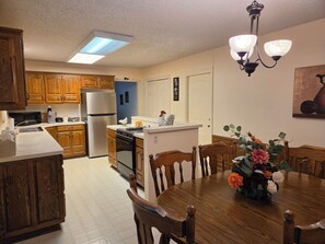 A kitchen with wooden cabinets, a refrigerator, a microwave, and a dining area with a wooden table and chairs. - West Gate Retreat 3 bedroom home near Desoto Golf Club in Hot Springs Village (Hot Springs)