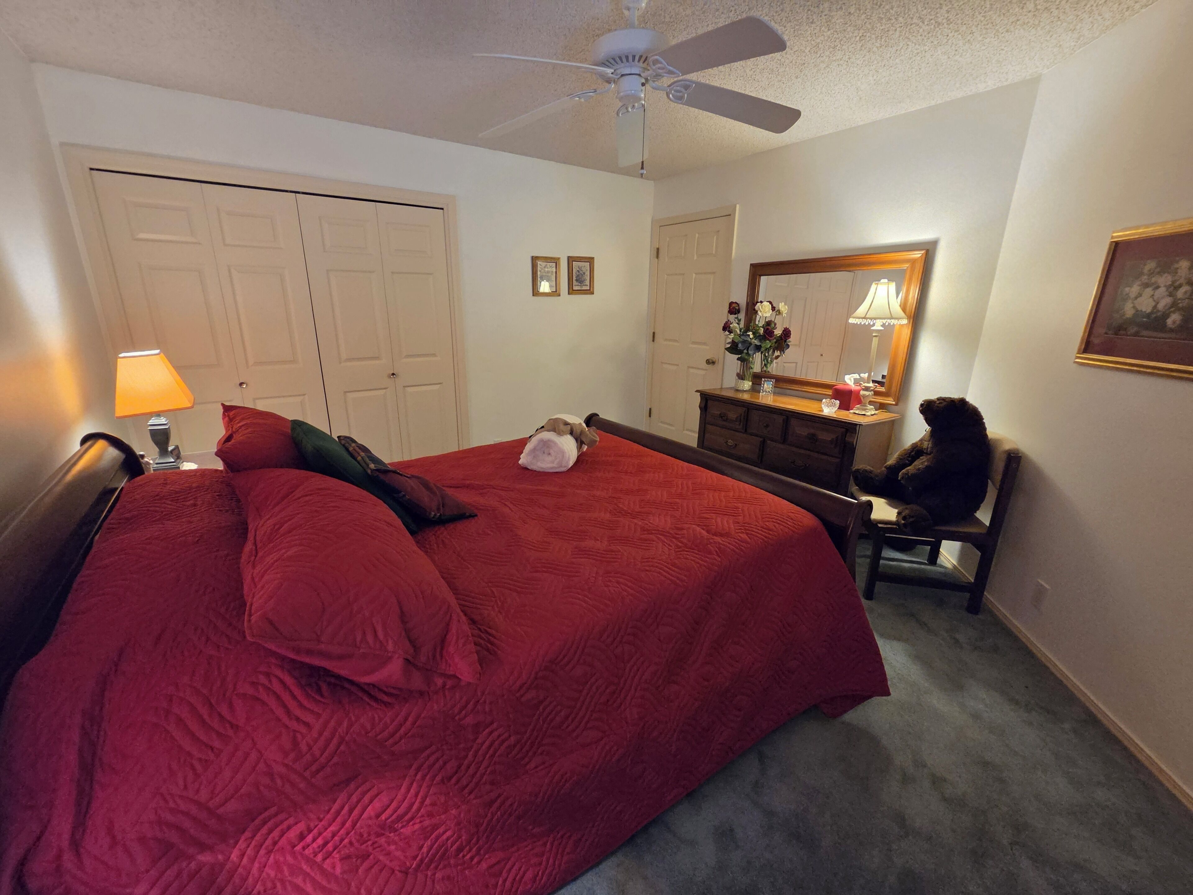 A bedroom with a bed, a dresser, a chair, a ceiling fan, and a mirror.