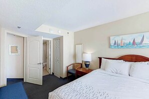 A hotel room with a bed, a desk with a lamp, a chair, and a painting on the wall. - Carolinian Beach Resort 0830 (Myrtle Beach)