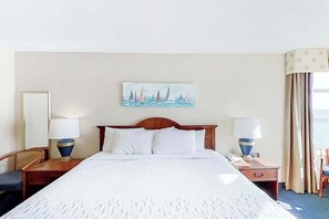 Ein Hotelzimmer mit einem großen Bett, zwei Nachttischen mit Lampen, einem Sessel und einem Gemälde an der Wand, sowie einem Fenster mit Vorhängen.