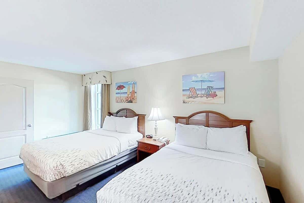 Ein Hotelzimmer mit zwei Betten, einer Tür, einem Fenster mit Vorhängen und zwei an der Wand befestigten Bildern.