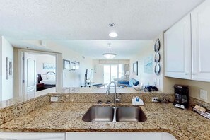 A kitchen with a double sink, granite countertop, and white cabinets. - Carolinian Beach Resort 0830 (Myrtle Beach)