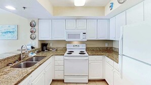 A kitchen with white cabinets, a microwave, a stove, and a refrigerator. - Carolinian Beach Resort 0830 (Myrtle Beach)