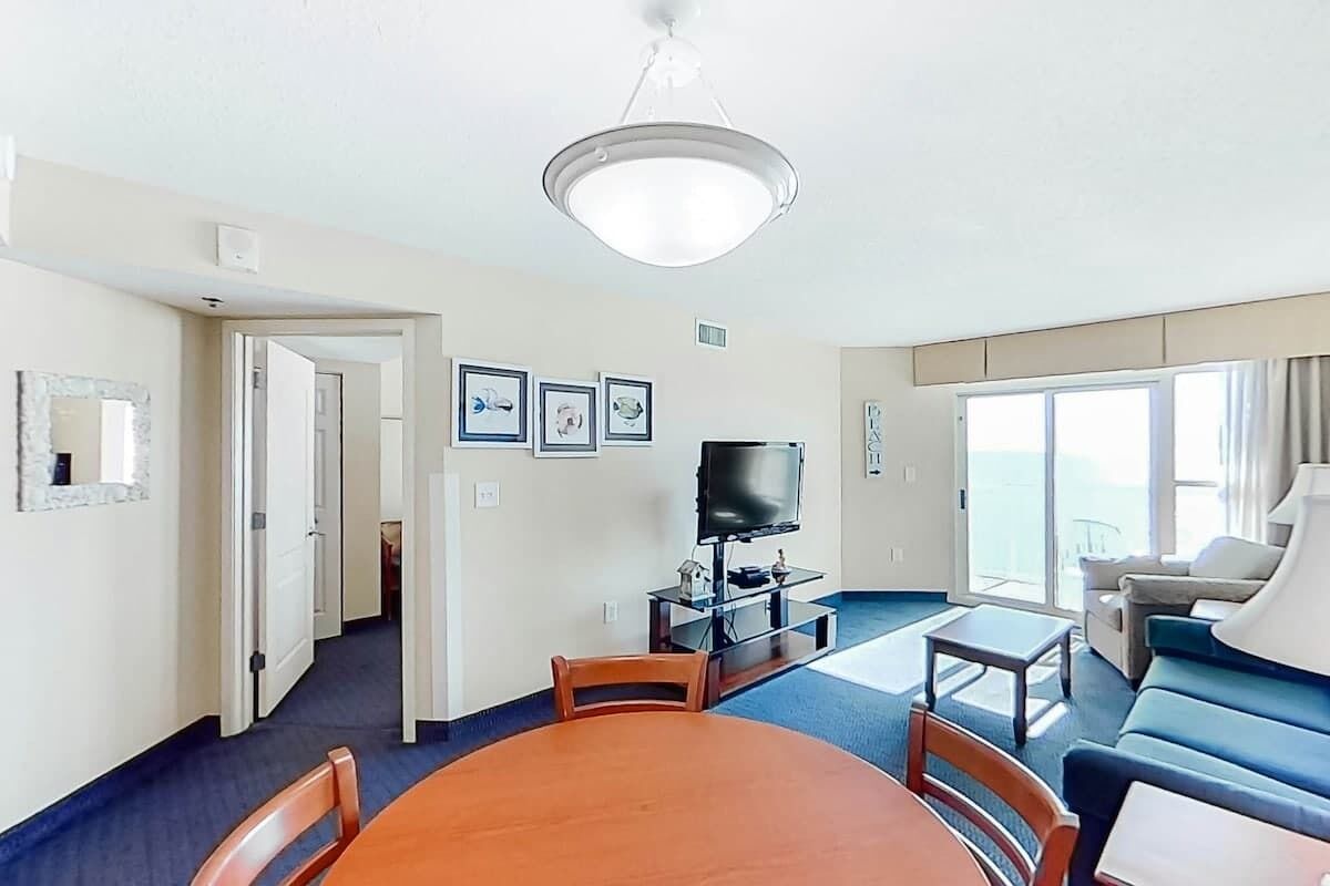 Ein Hotelzimmer mit Esstisch, Stühlen, Fernseher, Sofa und einem großen Fenster mit Blick.