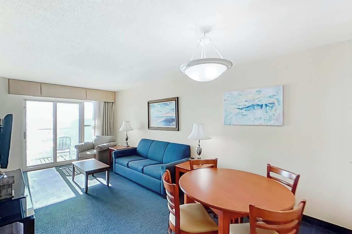Ein Hotelzimmer mit einer Couch, einem Esstisch mit Stühlen, einer Lampe und einem Bild an der Wand.
