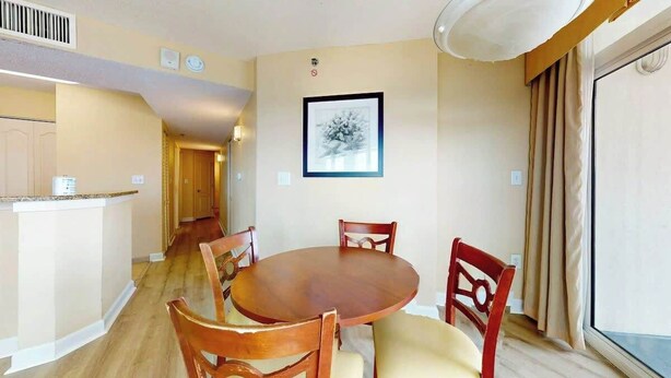 Ein Essbereich mit rundem Tisch und Stühlen, eine Küchenzeile mit einer Arbeitsplatte und ein großes Fenster mit Vorhängen.