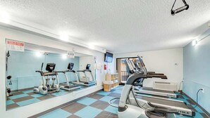 Ein Fitnessraum mit verschiedenen Cardiogeräten, einer Spiegelwand und einem Schachbrettmuster auf dem Boden.