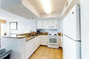 A kitchen with white cabinets, a stove, a microwave, and a refrigerator. - Carolinian Beach Resort 0831 (Myrtle Beach)