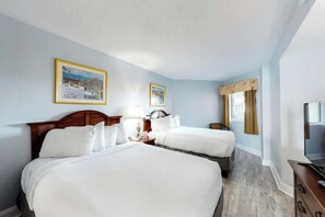 A hotel room with two beds, a wooden headboard, a TV, a lamp, and two framed pictures on the wall. - Carolinian Beach Resort 0831 (Myrtle Beach)