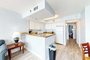 A modern kitchen with white cabinets, a granite countertop, and a small dining area with a table and chairs. - Carolinian Beach Resort 0831 (Myrtle Beach)