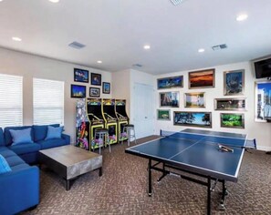 Una stanza con un tavolo da ping pong, giochi arcade, un divano blu e quadri appesi al muro.