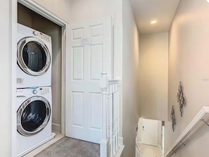 A laundry room with two front-loading washing machines, a white door with a decorative trim, and a staircase with a handrail. - Beautiful Vacation Home Near Disney  3BR 3BA Family Friendly (Clermont)