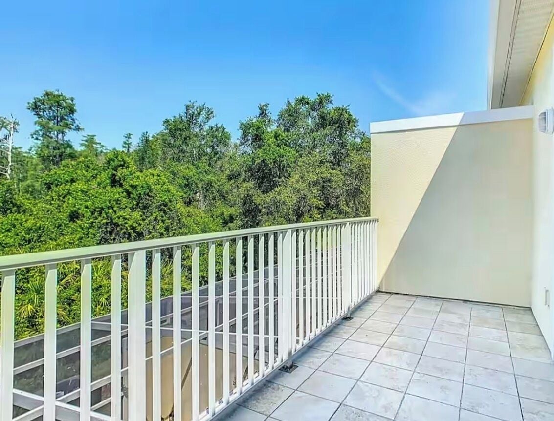 Un balcón con suelo de baldosas y baranda blanca, con vistas a una zona verde exuberante.