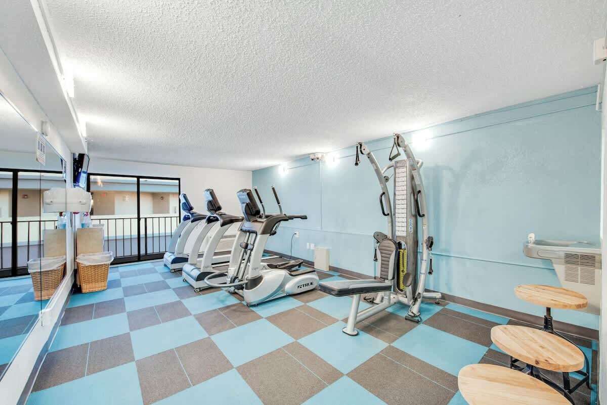 A gym with cardio machines, weight benches, and a mirrored wall.