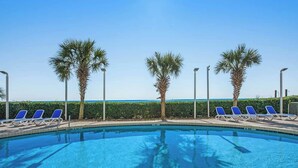 A swimming pool with lounge chairs and palm trees, with a view of the ocean. - Oceanview Penthouse 2134 (Myrtle Beach)