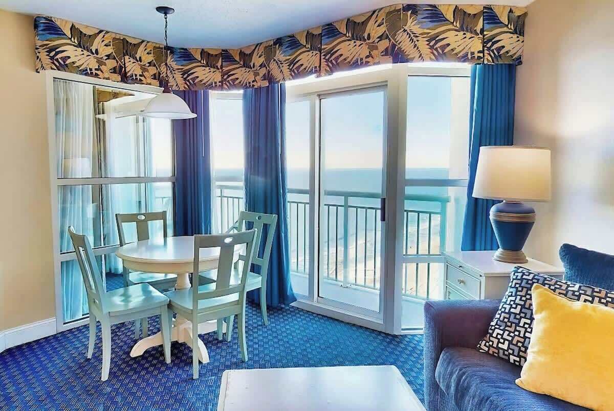 A room with a balcony, a dining table with chairs, a sofa, and a lamp.