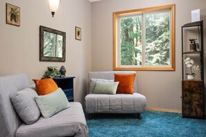 A room with two sofas, a window with a forest view, and a bookshelf.