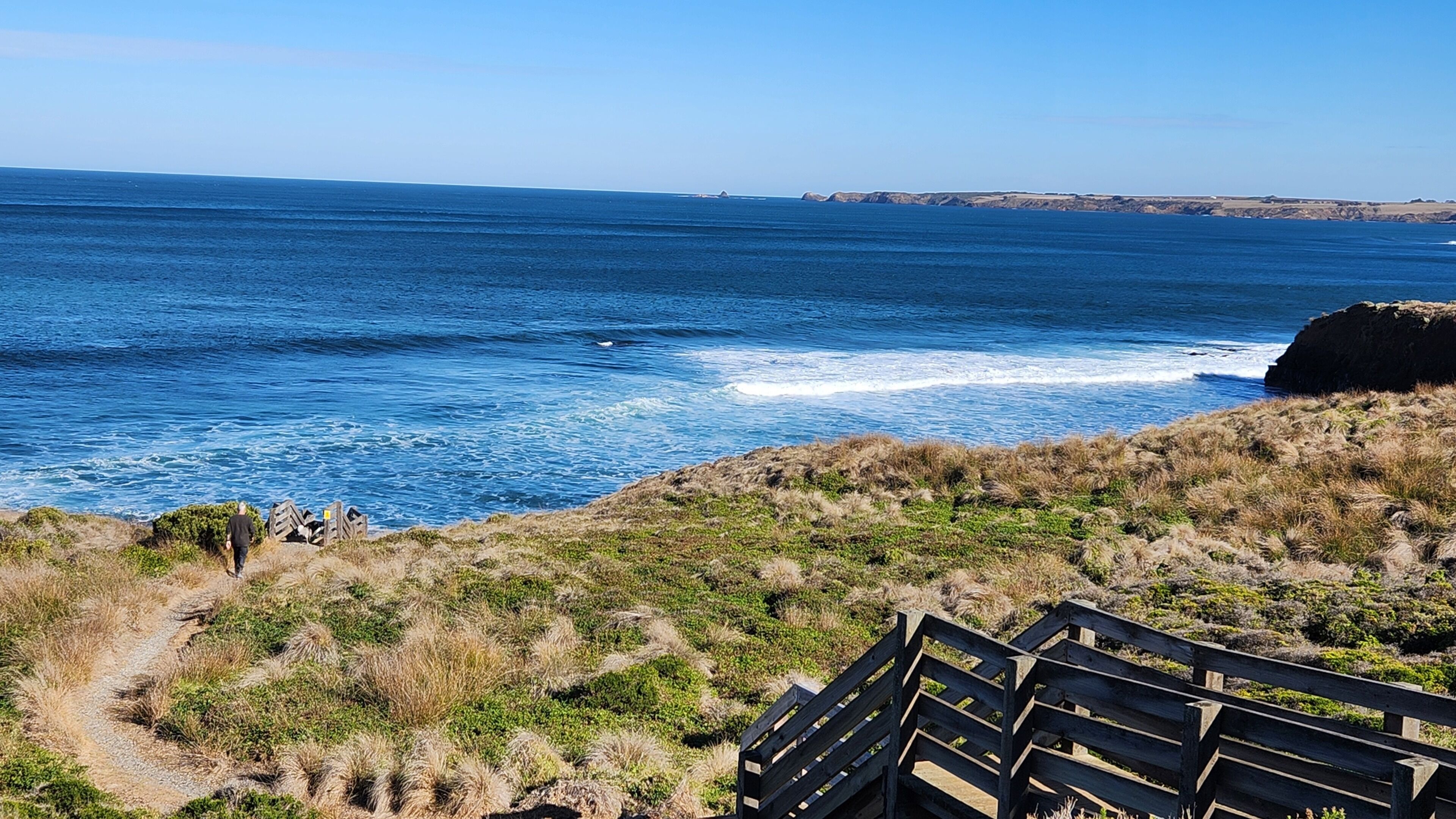 Paesaggio costiero con una passerella in legno che conduce a una scogliera con vista sull'oceano.