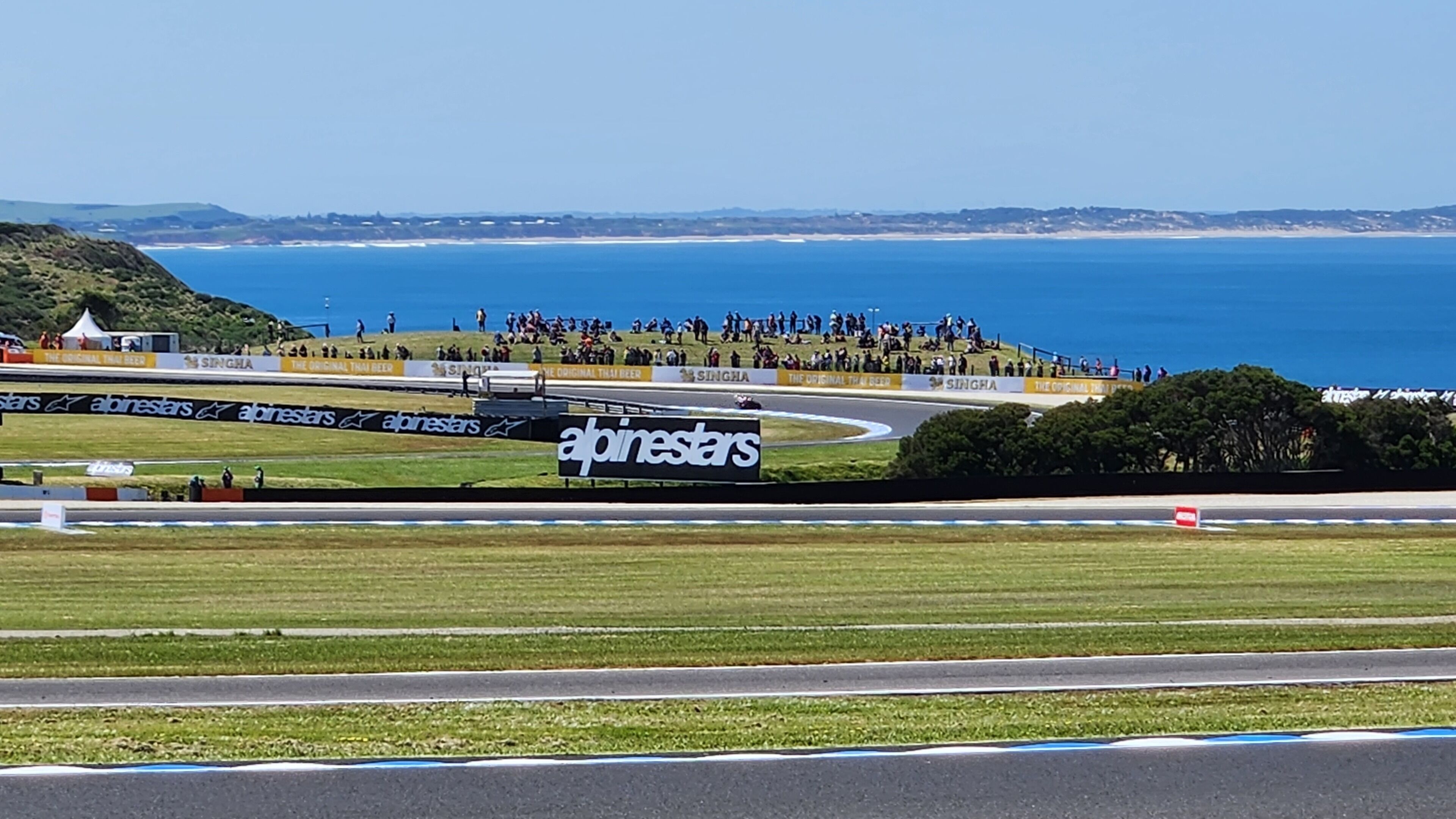 A race track with a large billboard advertising 'alpinestars' and a crowd of spectators.