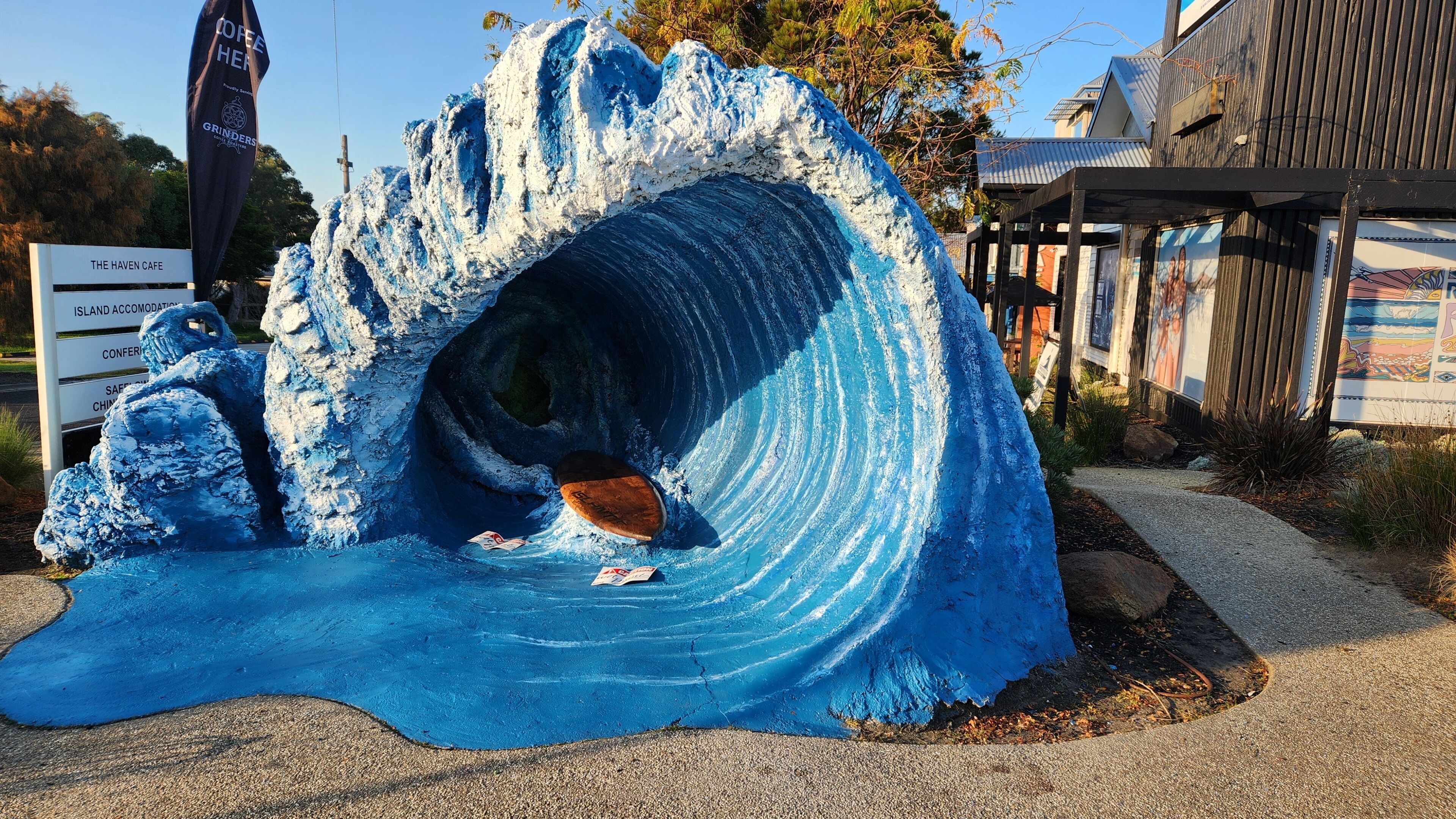 A wave-shaped structure with a wooden bench inside, surrounded by a gravel area.