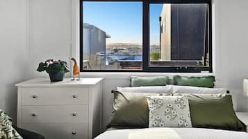 A bedroom with a bed, a nightstand, a dresser, a window with a view of buildings, and a lamp.