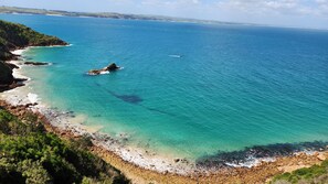 A coastal landscape with clear turquoise waters, rocky shoreline, and distant hills.