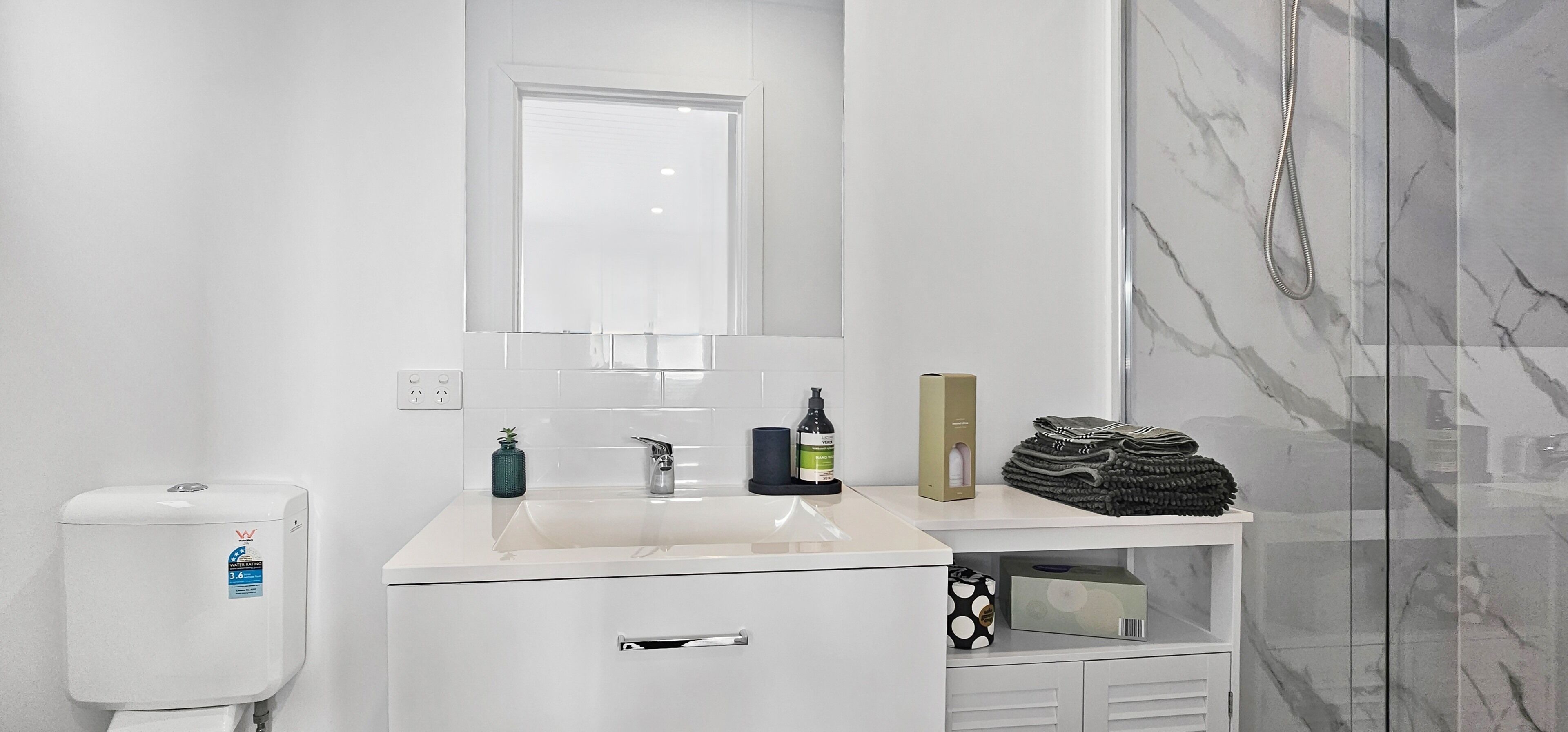 A modern bathroom with a white sink, a mirror, a toilet, and a glass shower enclosure.