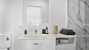 A modern bathroom with a white sink, a mirror, a toilet, and a glass shower enclosure.