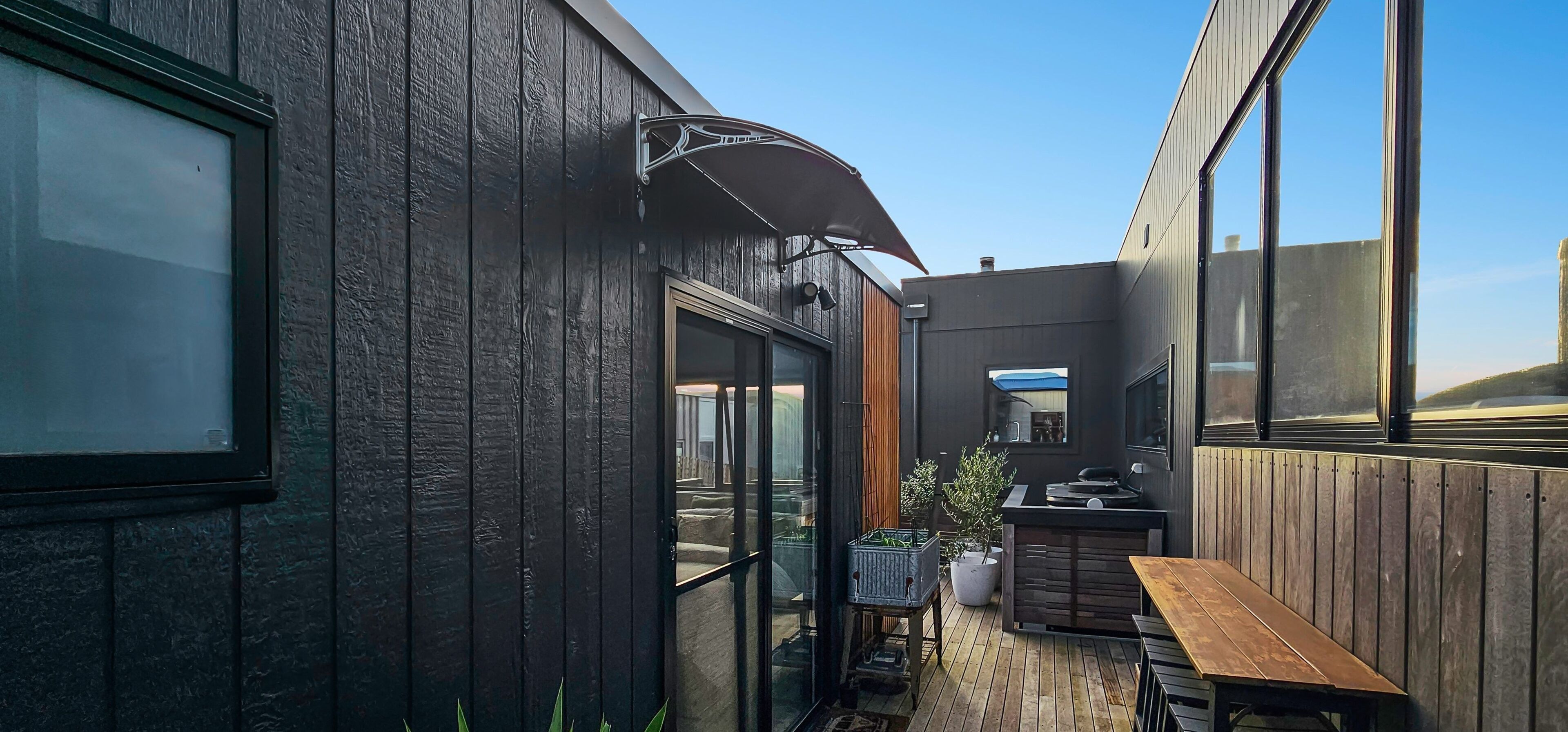 A wooden building with large windows, a patio with a table and chairs, and a small garden area.