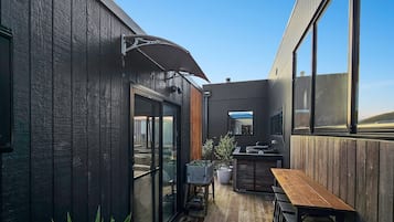 A wooden building with large windows, a patio with a table and chairs, and a small garden area.