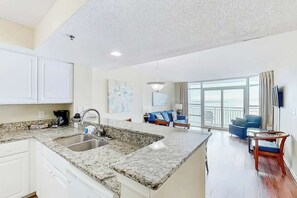 A modern kitchen with granite countertops, a double sink, and a dining area with a view of the ocean. - Carolinian Beach Resort 0832 (Myrtle Beach)