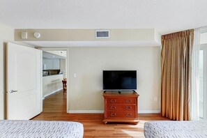 A hotel room with a television on a wooden dresser, a door leading to a kitchen, and a window with curtains. - Carolinian Beach Resort 0832 (Myrtle Beach)