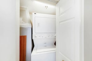 A compact laundry room with stacked appliances, including a dryer and a washing machine. - Carolinian Beach Resort 0832 (Myrtle Beach)