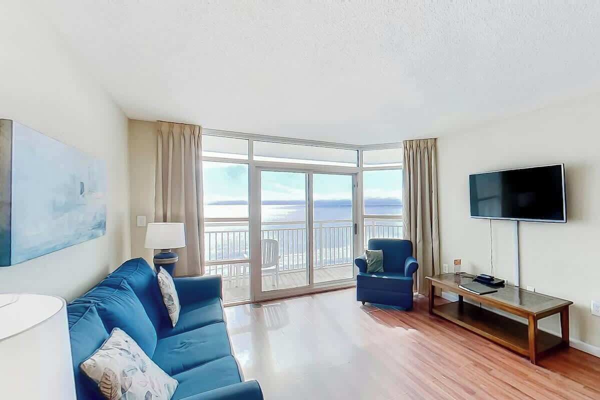 Ein Wohnzimmer mit einem blauen Sofa, einem Fernseher und einem Balkon mit Blick.