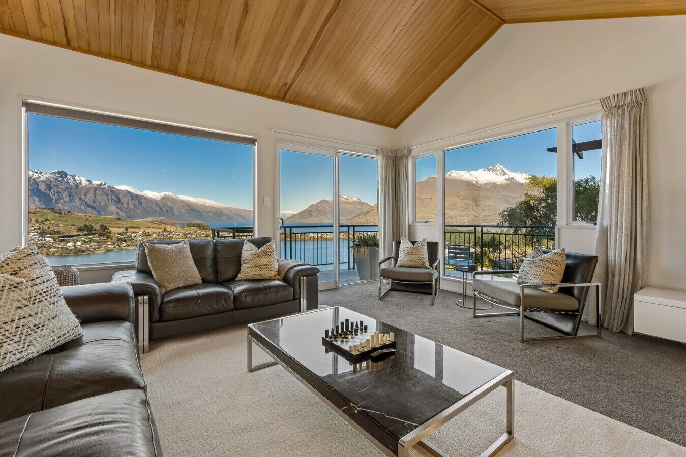 A spacious living room with a large window offering a mountain view, a leather sofa, a glass coffee table, and a seating area with a view.