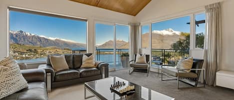 A spacious living room with a large window offering a mountain view, a leather sofa, a glass coffee table, and a seating area with a view.