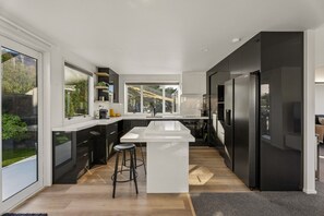 A modern kitchen with a central island, black cabinetry, and large windows. - Panorama Point - Amazing Views & Location (Queenstown)