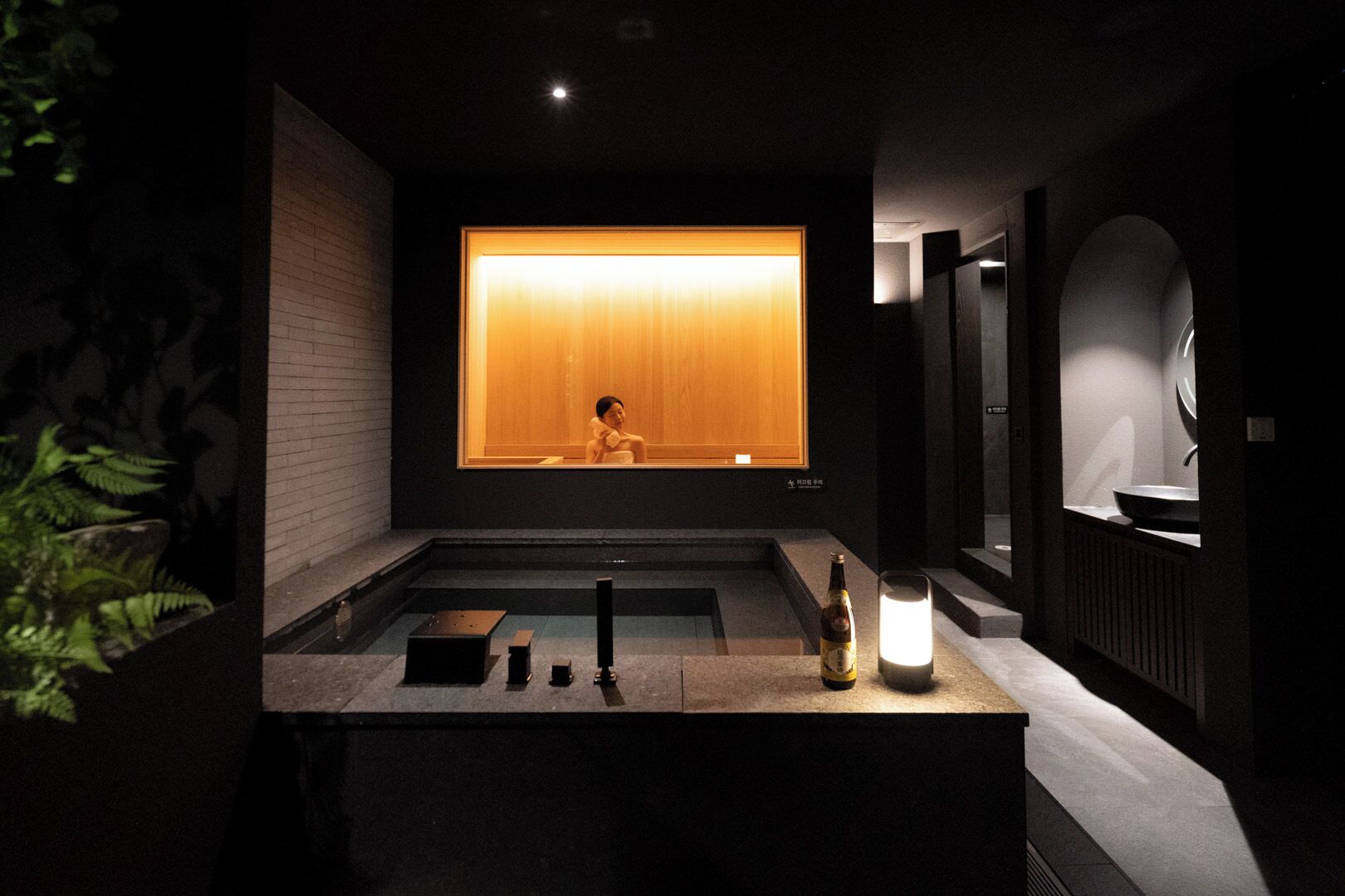 A modern bathroom with a large window, a bathtub, a sink, and a mirror.