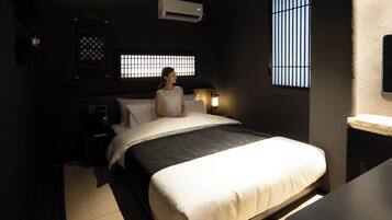 A bedroom with a bed, bedside table, lamp, and a window with bars.