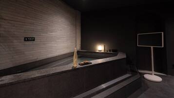 Ein modernes Badezimmer mit Backsteinwand, einer Badewanne, einem kleinen Tisch mit Flasche und Keksen sowie einem Schild in einer Fremdsprache.