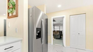 A kitchen with a stainless steel refrigerator, a white countertop, and a door leading to a living area. - Heated Pool No Extra Fee ! firepit| Game Room (Palm Coast)