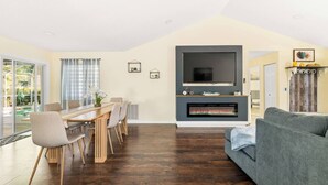 A living room with a fireplace, a dining area with a table and chairs, and a grey sofa. - Heated Pool No Extra Fee ! firepit| Game Room (Palm Coast)
