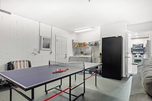 Ein Zimmer mit Tischtennisplatte, Waschmaschine, Trockner und einer Küchenzeile mit Geräte.