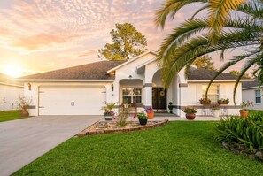 A single-story house with a garage, a front porch with potted plants, and a well-maintained lawn. - Heated Pool No Extra Fee ! firepit| Game Room (Palm Coast)
