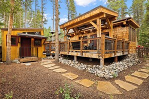 A wooden cabin with a deck, surrounded by a stone pathway and a forest. - NEW! Magical home in prime neighborhood (Breckenridge)