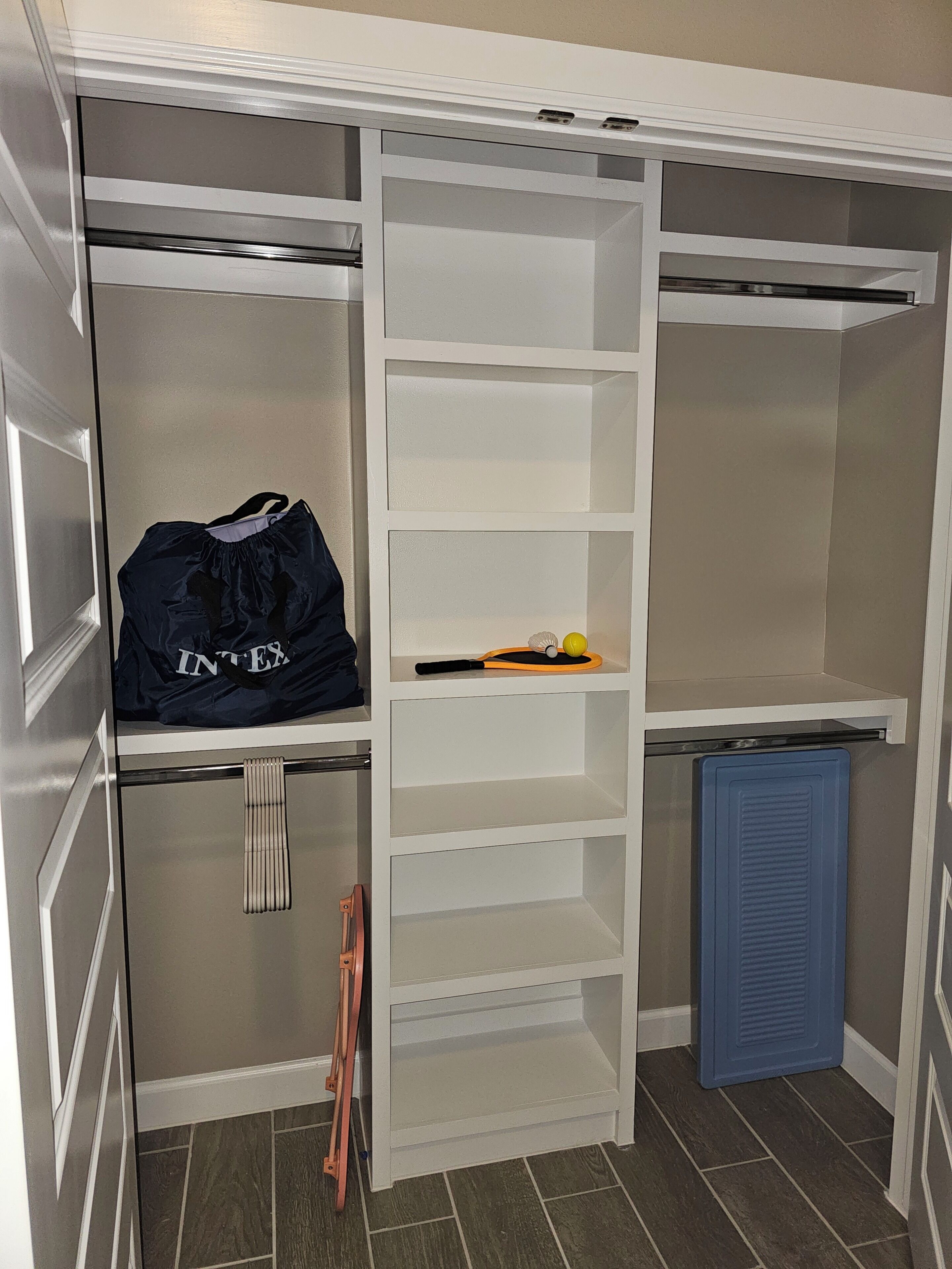 Ein begehbarer Kleiderschrank mit mehreren Regalen und Kleiderstangen, eine blaue Aufbewahrungsbox und eine Leiter.