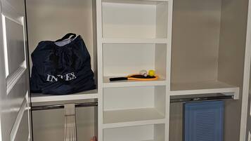 Ein begehbarer Kleiderschrank mit mehreren Regalen und Kleiderstangen, eine blaue Aufbewahrungsbox und eine Leiter.