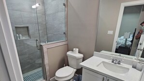 Et moderne badeværelse med et brusebad bag glas, et toilet, en vask med et spejl og en tæppe med et mønster.