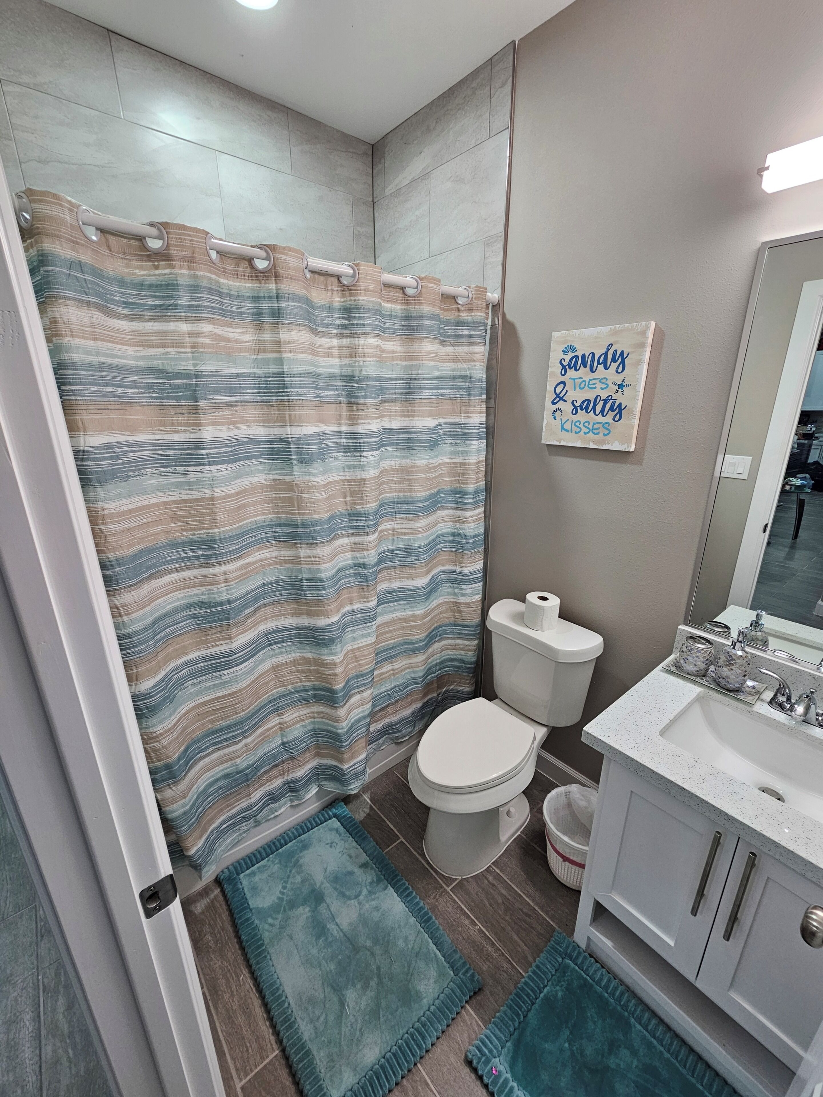 Un bagno con tenda da doccia a righe, un water, un lavandino con uno specchio e un cartello fissato al muro.