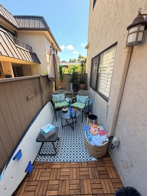 Eine Terrasse mit einem gemusterten Boden, Gartenmöbeln und einem Surfbrett, das an der Wand lehnt.